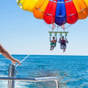 Happy couple Parasailing on Miami Beach in summer. Couple under parachute hanging mid air. Having fun. Tropical Paradise. Positive human emotions, feelings, family, travel, vacation.
