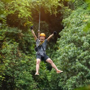 Freedom Man Tourist Wearing Casual Clothing On Zip Line Or Canopy Experience In Laos Rainforest, Asia