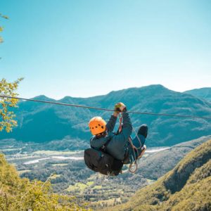 Young black male soaring through mountain peaks on an exhilarating zip-line adventure embracing nature's grandeur with breathtaking views and adrenaline-pumping thrills.