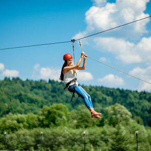 Young woman in casual wearing with red helmet riding on a zip line in the mountains. Active kind of recreation